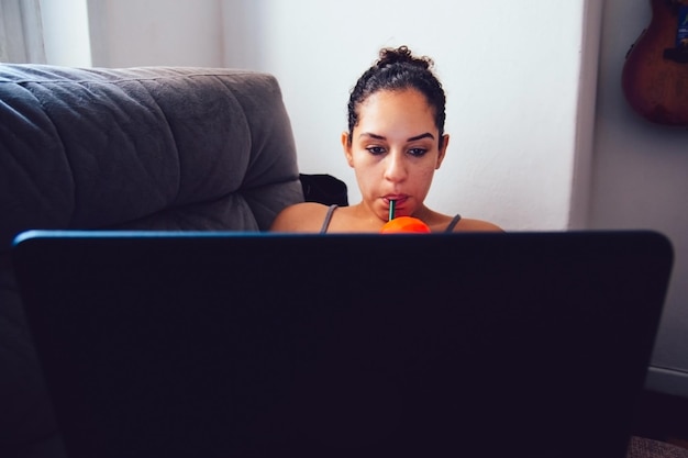 Mujer usando una computadora portátil mientras se desliza una bebida en casa