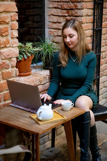 Mujer usando una computadora portátil mientras está sentada en una cafetería en la acera