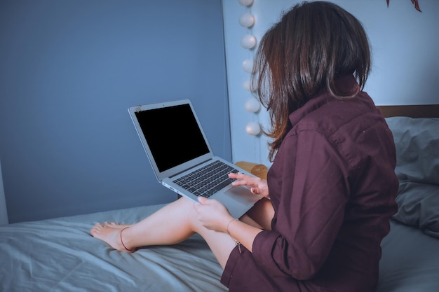 Mujer usando una computadora portátil mientras está sentada en la cama en casa