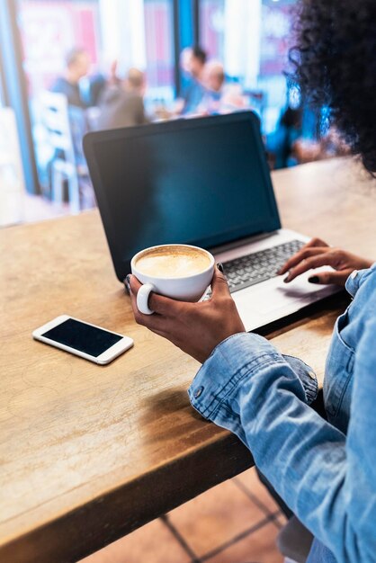 Foto mujer usando una computadora portátil mientras toma café en una cafetería