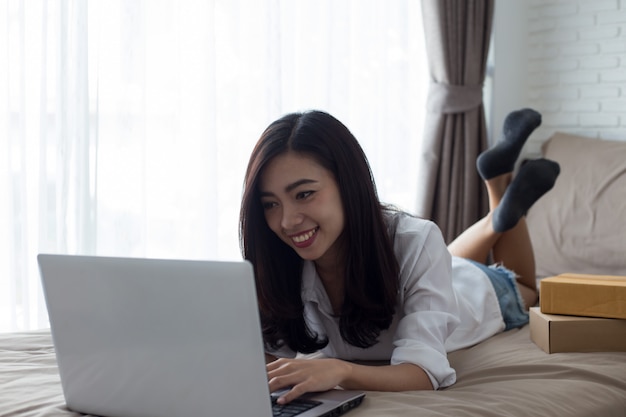 Mujer usando una computadora portátil en su cama, en la habitación blanca junto a la ventana, compras en línea concep