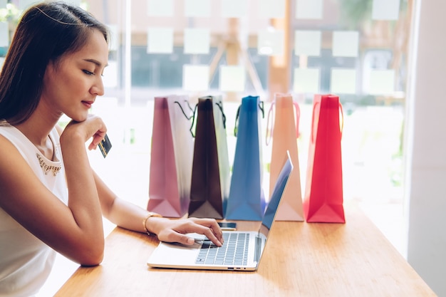 Mujer usando computadora y tarjeta de crédito para pago en línea con bolsas de compras en la mesa