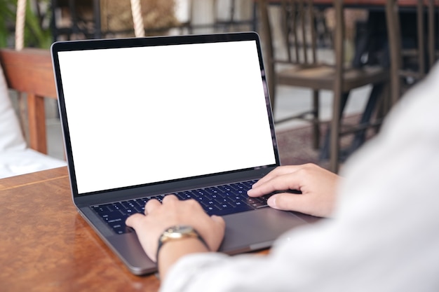 Mujer usando y escribiendo en la computadora portátil con pantalla en blanco en la mesa de madera