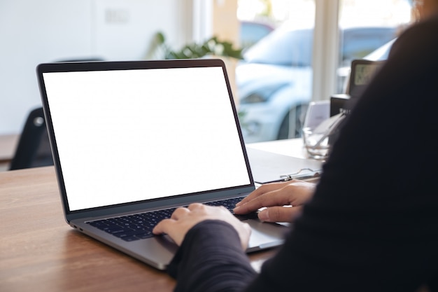 Una mujer usando y escribiendo en una computadora portátil con pantalla de escritorio en blanco mientras está sentado en la oficina