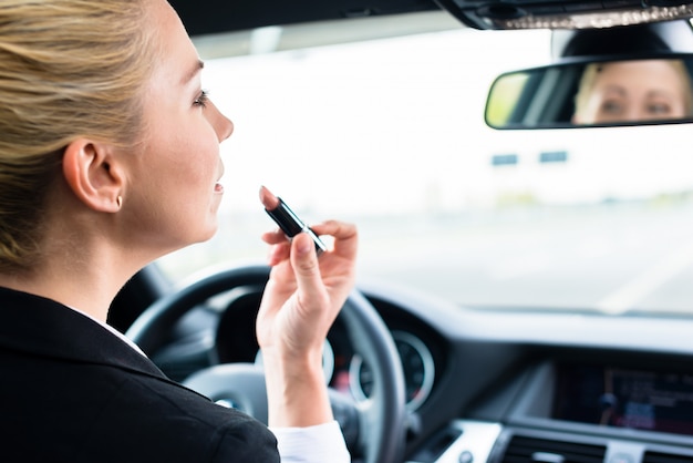 Mujer usando lápiz labial mientras conduce su auto