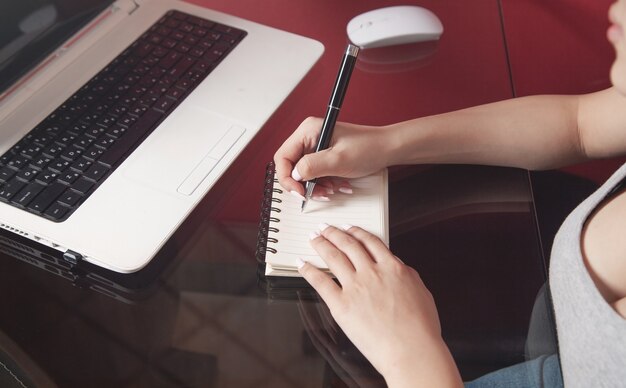 Mujer usando laptop y escribiendo en un bloc de notas.