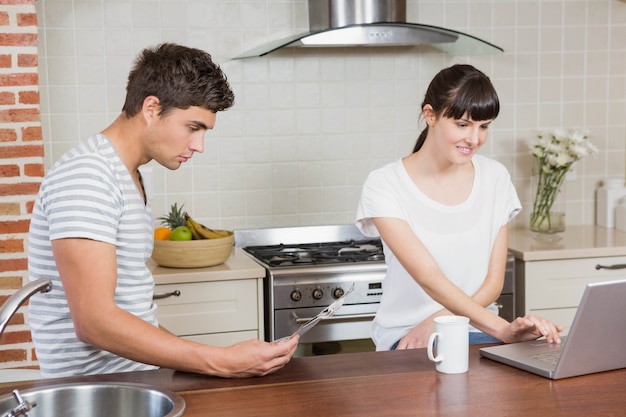 Mujer usando laptop y hombre leyendo el periódico en la cocina