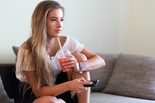 Mujer usando una pajilla para beber jugo de toronja mientras mira televisión