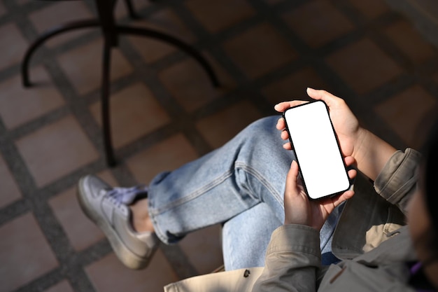 Una mujer usando su teléfono inteligente mientras se relaja sentada en la maqueta de la pantalla blanca del teléfono del café