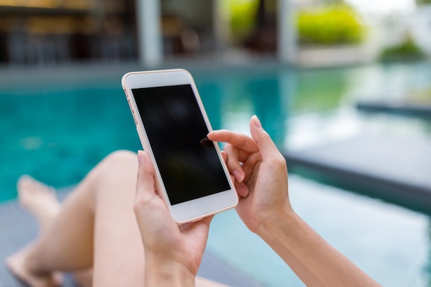 Mujer usando su teléfono móvil y relajándose en la piscina