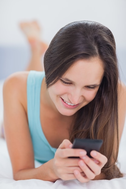 Foto mujer usando su teléfono y sonriendo mientras está en la cama