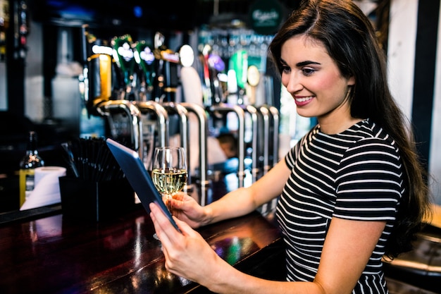 Mujer usando tableta y tomando una copa de vino en un bar