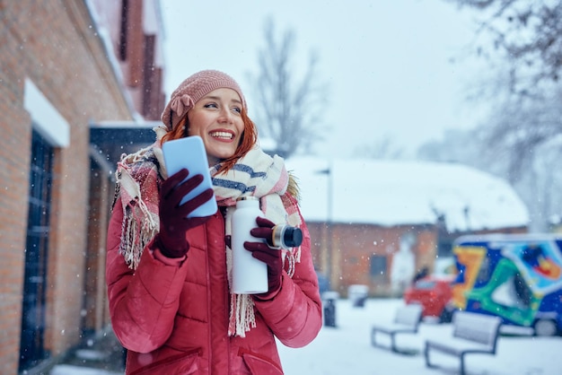 Mujer usando teléfono y bebiendo bebidas calientes al aire libre