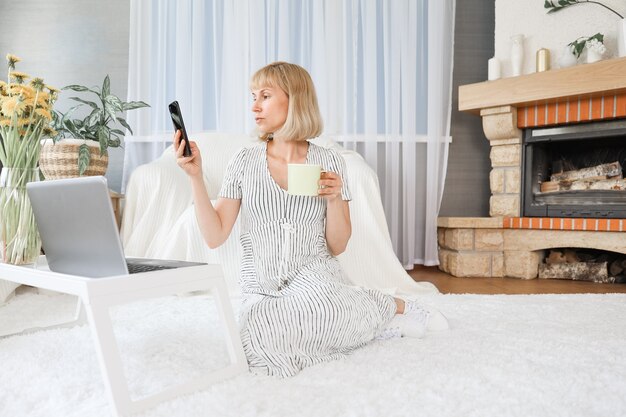 Mujer usando un teléfono y una computadora portátil en casa