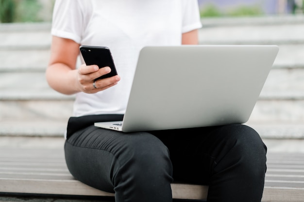 Mujer usando teléfono y computadora portátil en el parque