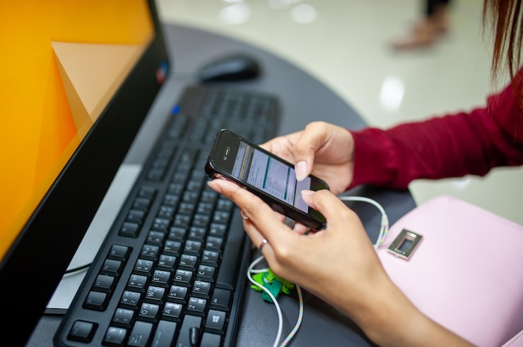 Foto mujer usando teléfono inteligente mientras está sentada en el escritorio con la configuración de la computadora