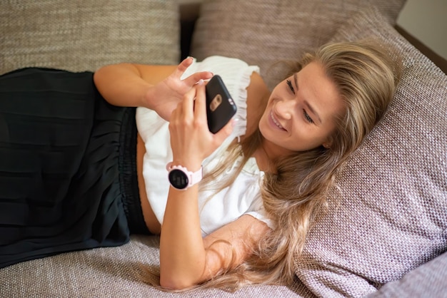 Mujer usando un teléfono inteligente mientras se relaja en el sofá