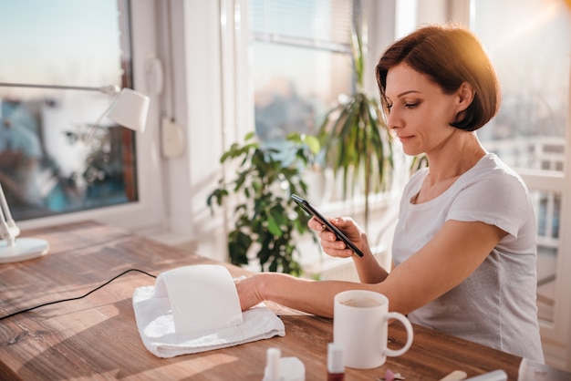 Mujer usando un teléfono inteligente mientras se seca las uñas