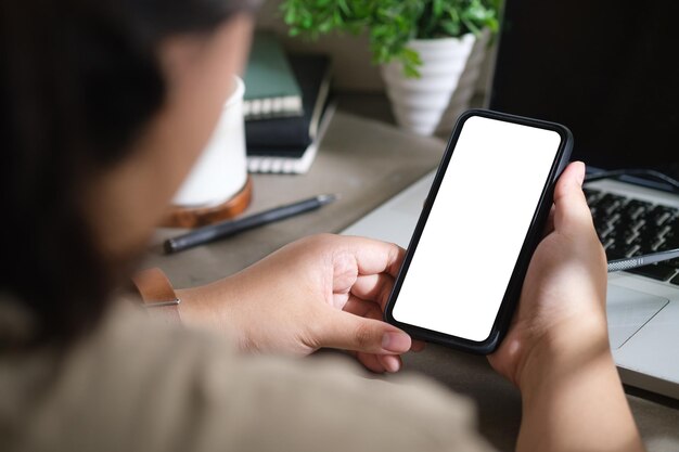 Mujer usando un teléfono inteligente mientras se sienta frente a la computadora portátil en el escritorio de la oficina