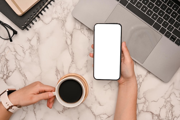 Mujer usando un teléfono inteligente mientras toma un café en su moderno espacio de trabajo de mármol blanco