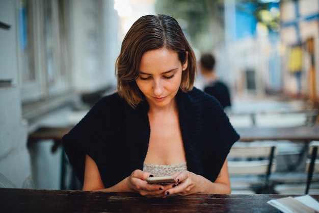 Mujer usando el teléfono mientras está sentada en una cafetería al aire libre