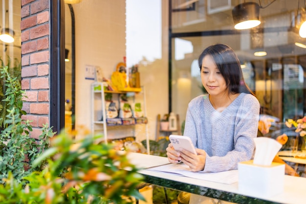 Mujer usando el teléfono móvil en un café con reflejo en la ventana