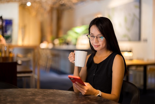 Mujer usando el teléfono móvil en la cafetería por la noche
