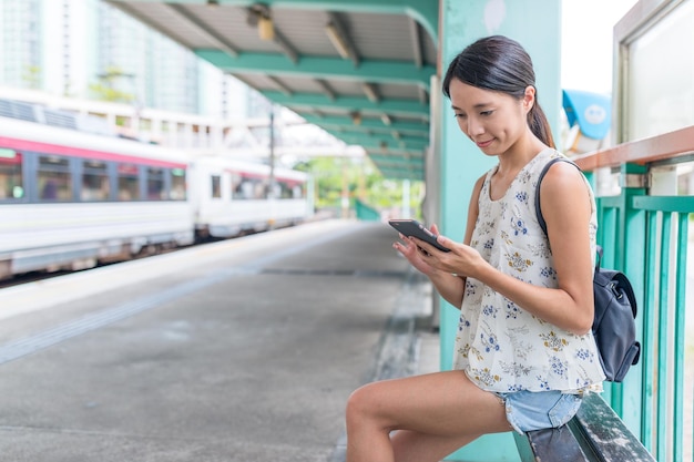 Mujer usando teléfono móvil y esperando en la estación trsin