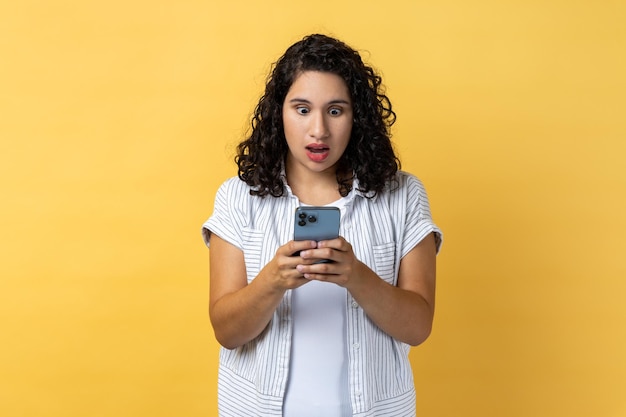 Mujer usando teléfono móvil y leyendo noticias impactantes en noticias sociales mirando la pantalla con ojos grandes