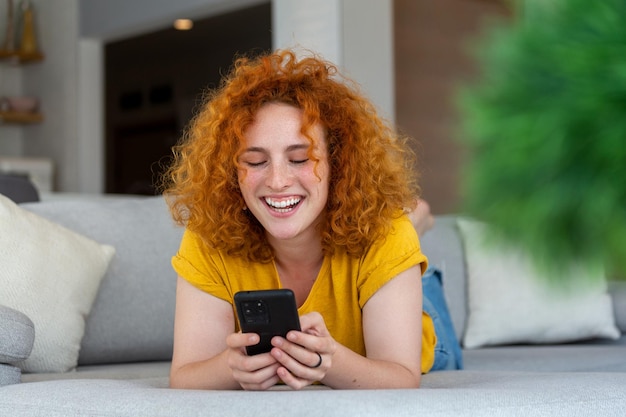 Mujer usando teléfono móvil mientras está acostada en el sofá Mujer joven está descansando en casa