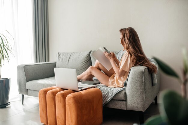 Mujer usando teléfono móvil mientras está sentada en el sofá en casa