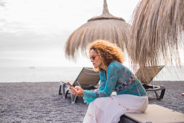 Foto mujer usando teléfono móvil mientras está sentada en la playa