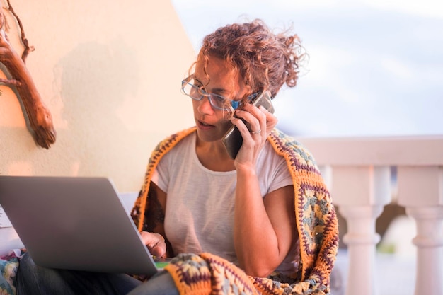 Mujer usando teléfono móvil y portátil mientras está sentada en casa