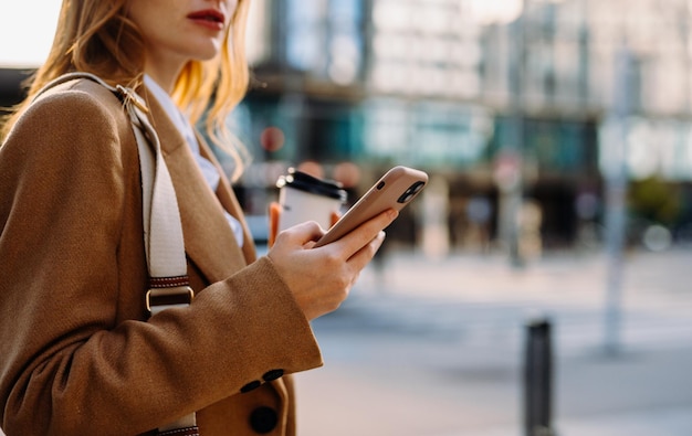 Mujer usando teléfono sosteniendo café con edificios residenciales borrosos de la ciudad en el fondo como