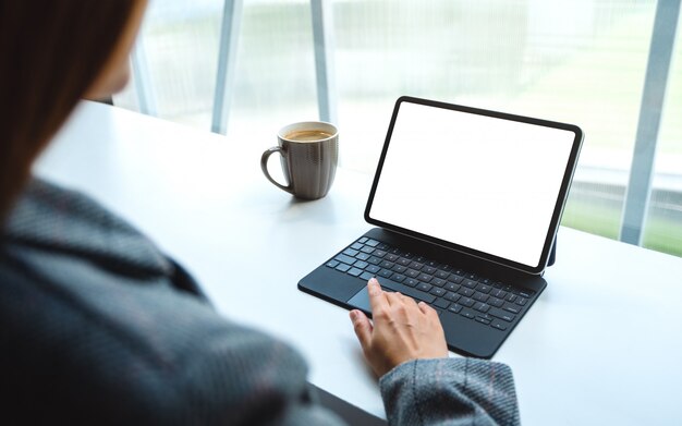 de una mujer usando y tocando el panel táctil de la tableta con una pantalla de escritorio blanca en blanco como PC, taza de café sobre la mesa