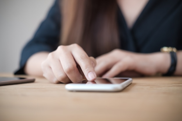 una mujer usando y tocando el teléfono inteligente en la mesa de madera