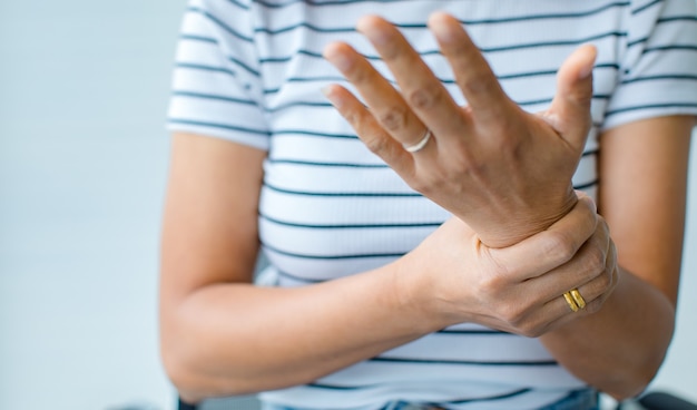 Mujer en el uso de la mano para sostener la muñeca y estirar los dedos con dolor, sufrimiento, dolor y hormigueo. Concepto de síndrome de Guillain barre y enfermedad de manos entumecidas.