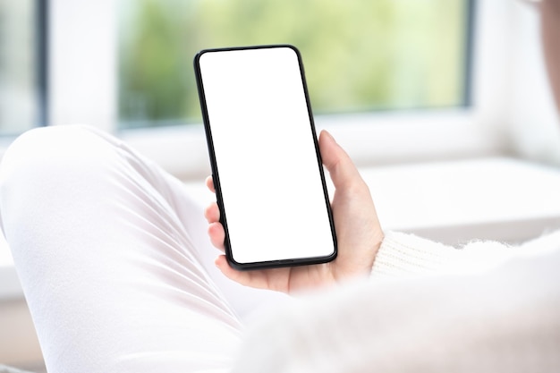 Mujer usuaria cliente sostiene maqueta de teléfono celular con pantalla blanca en mano maqueta de pantalla blanca en blanco de teléfono móvil con ropa blanca