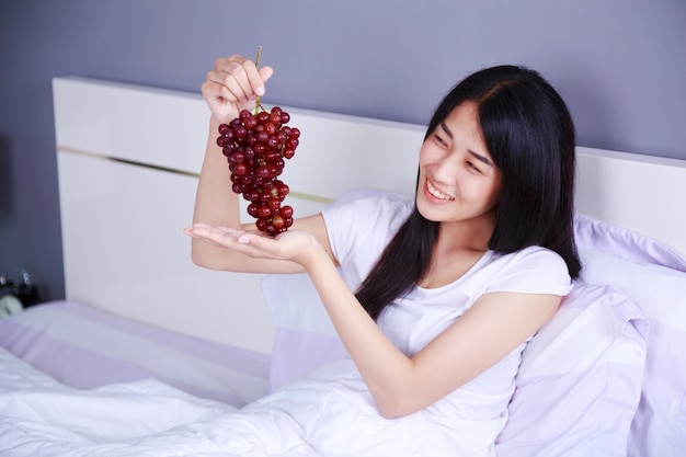 mujer con uva roja en la cama en el dormitorio