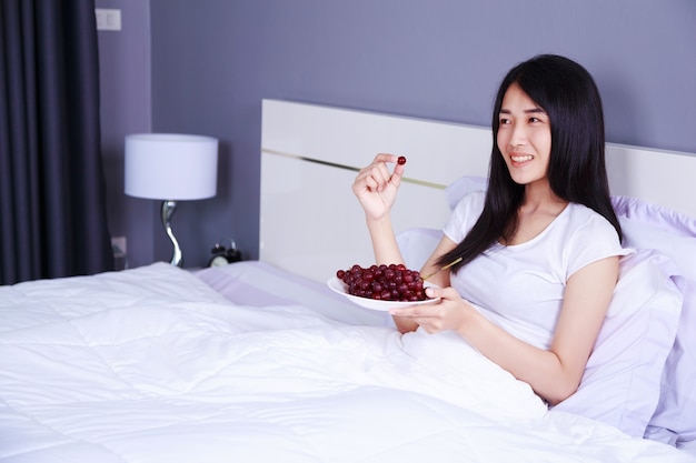 mujer con uva roja en la cama en el dormitorio