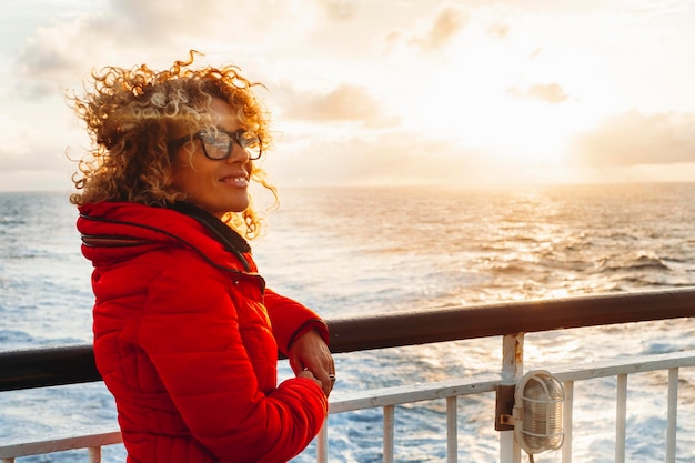 Mujer de vacaciones en crucero disfrutando de la puesta de sol en un viaje en el mar Mujer feliz viajera con chaqueta roja mirando el océano relajándose en un crucero de lujo Transporte de personas y transbordadores Actividad de viaje