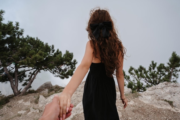 Una mujer valiente que guía a un viajero de la mano por un terreno rocoso salvaje. paisaje de montaña bajo el cielo