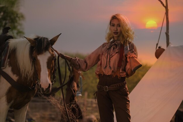 Foto mujer vaquera asiática cuidando amorosamente su arma y su caballo mientras está en el campamento al atardecer