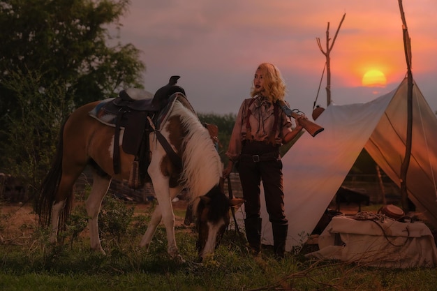 Foto mujer vaquera asiática cuidando amorosamente su arma y su caballo mientras está en el campamento al atardecer