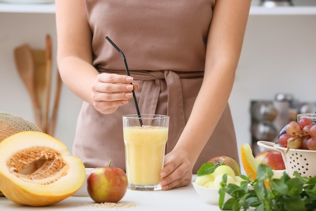 Mujer y vaso con batido de melón en la mesa de la cocina