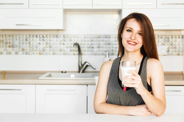 Mujer con vaso de leche en la cocina blanca