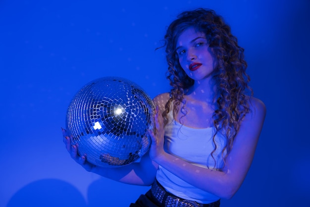 Foto la mujer se ve absolutamente impresionante mientras posa con una pelota de discoteca en las luces de neón de la fiesta azul del club nocturno