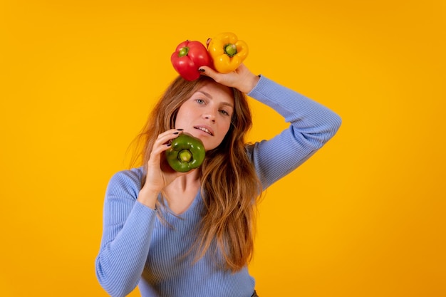 Mujer vegana con pimientos verdes amarillos y rojos sobre un fondo amarillo vida vegetariana