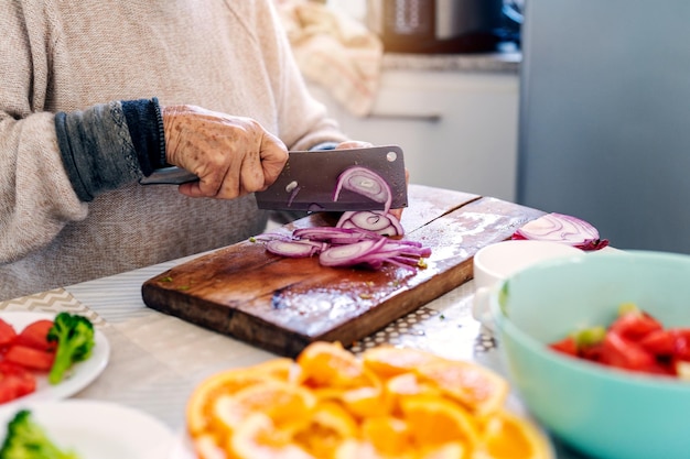 Mujer vegana senior cortando cebolla y preparando ensalada en tabla de cortar de maderax9