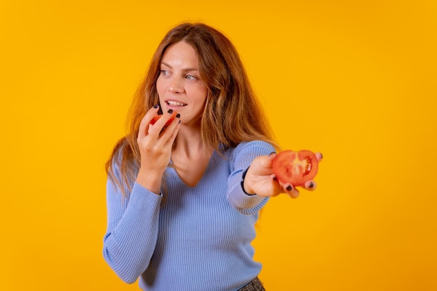 Mujer vegana sonriendo sosteniendo un tomate cortado sobre un fondo amarillo